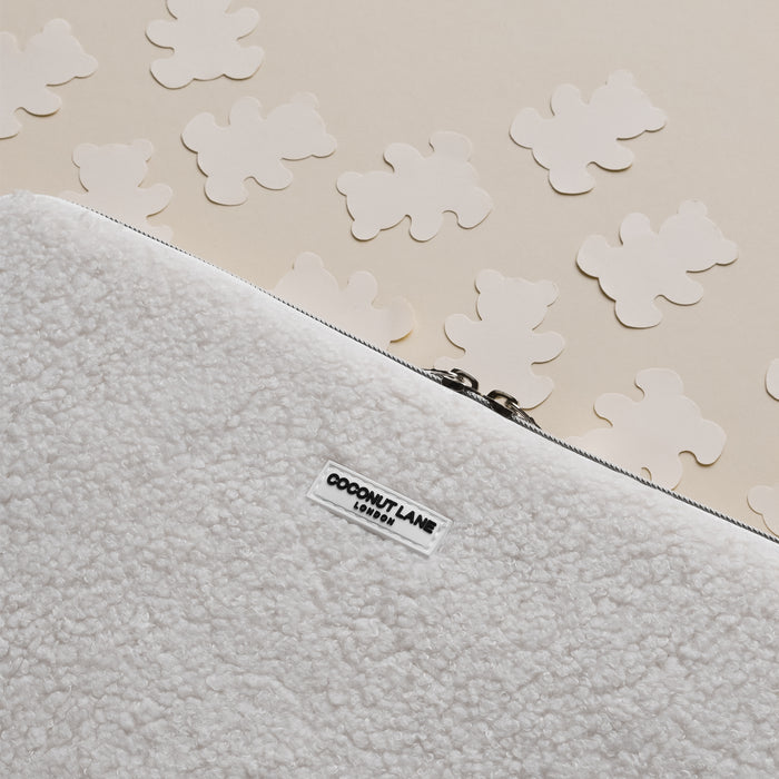 White fluffy Teddy Dolly laptop sleeve with zipper, beside bear-shaped cutouts on a beige surface.