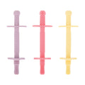 Nuby’s Tube Teethers (3 Pack) in purple, pink, and yellow stand upright on a white background. Each teether features cross-guards and a ribbed surface for easy grip, making them perfect for soothing little gums.