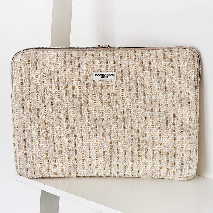 Cream and gold textured tweed laptop sleeve with zipper, placed on a white shelf.