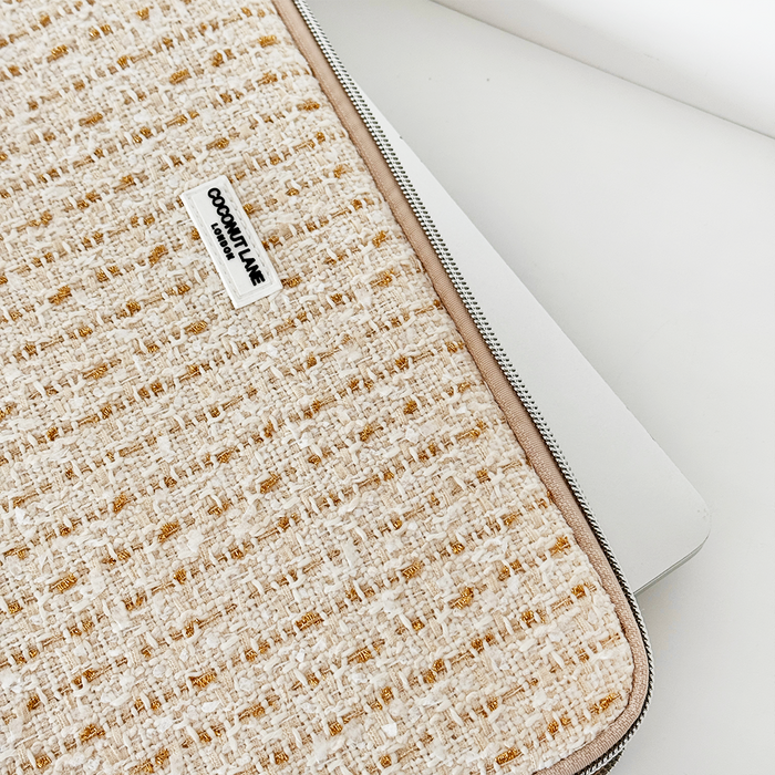 Silver laptop partially in a vanilla textured tweed sleeve with visible Coconut Lane label and fabric detail.
