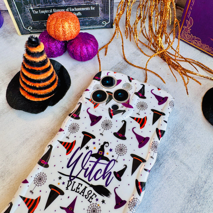 Witch Please Wavy Luxe MagSafe iPhone case laid flat beside an orange striped witch hat and purple pumpkins on a white surface.